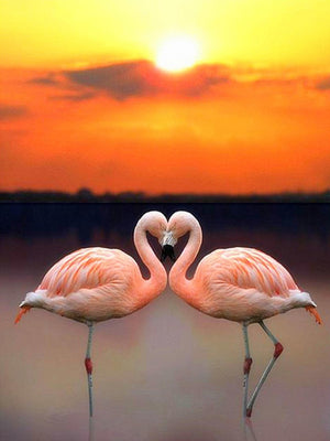 Diamond painting af to lyserøde flamingoer, der danner et hjerte i solnedgangens orange farver.