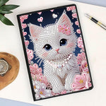 Diamond art notesbog med læder, blanke sider og en vid kat omgivet af rosa blomster på forsiden.