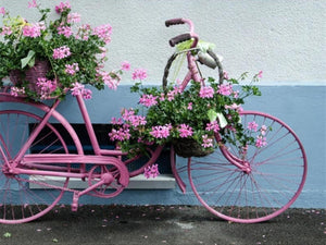 Diamond paint af en parkeret lyserød cykel med kurve fyldt med lyserøde blomster.