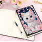 Diamond painting notesbog i læder med hvid kat og lyserøde blomster. Blanke sider.