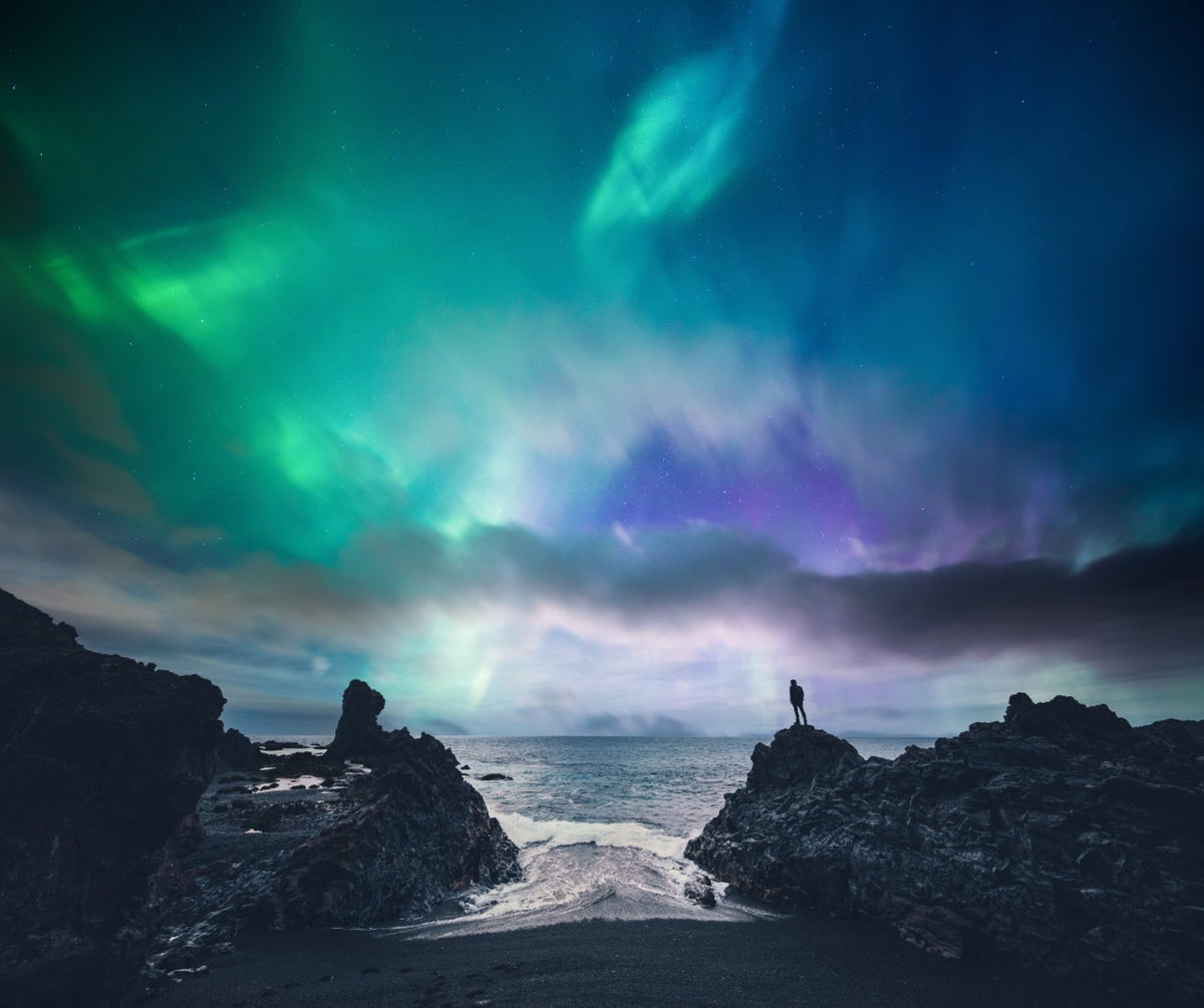 Diamond painting af nordlys mellem klipper over havet.